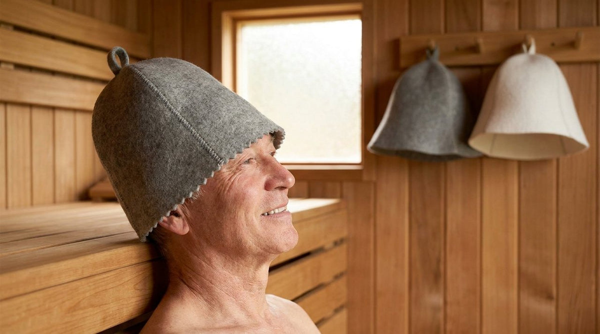Older man relaxing in a cedar sauna wearing a grey wool felt sauna hat, calm light