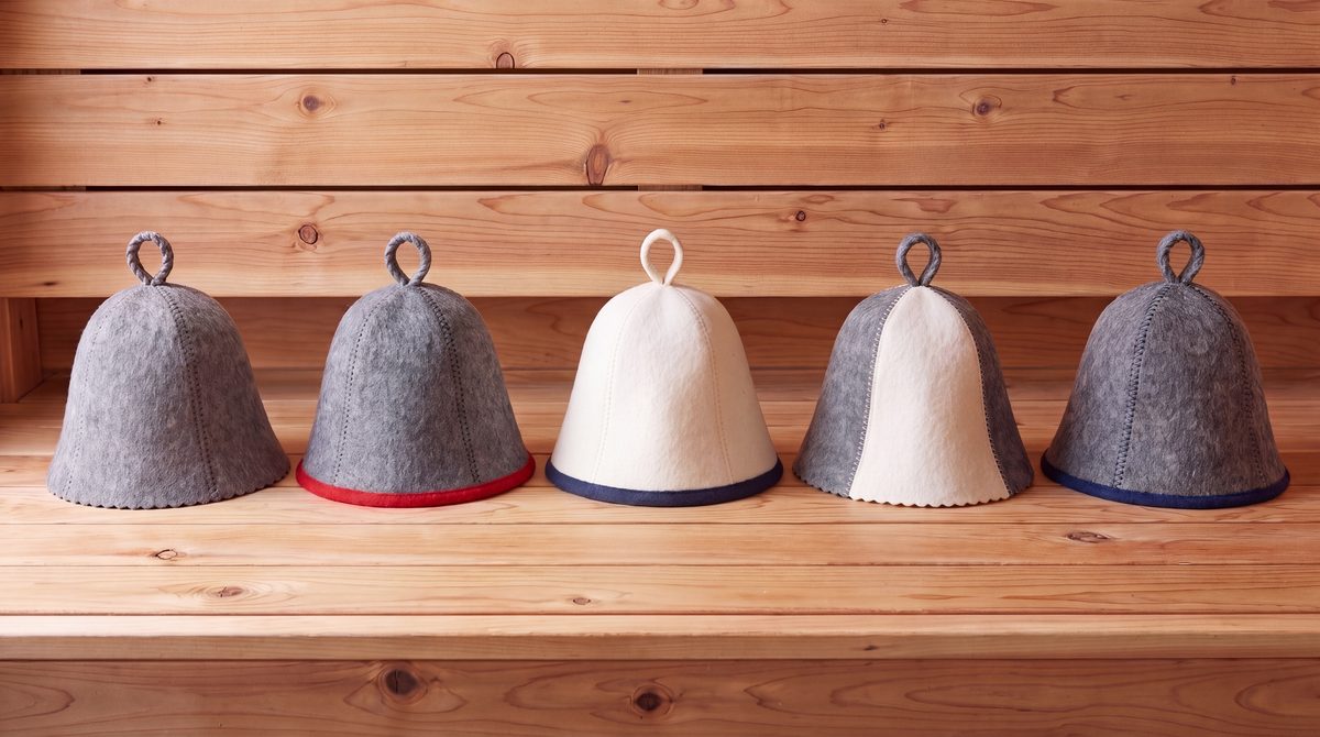 Five wool felt sauna hats in different colors on a cedar sauna shelf: grey, grey-red, white-blue, white-grey and grey-blue