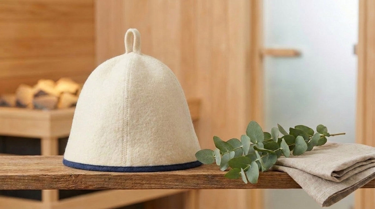 Elegant white wool sauna hat with blue trim on wooden shelf with eucalyptus sprig, spa aesthetic