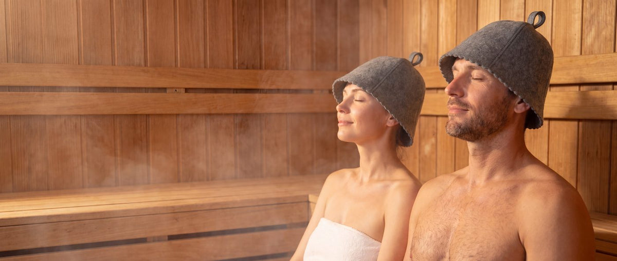 Couple in a cedar sauna wearing grey DIVELUX wool sauna hats